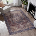 A distressed vintage-style area rug with a faded medallion pattern in muted purple, beige, and brown tones, styled on a light wood floor in a bright living room next to a white armchair and fireplace.